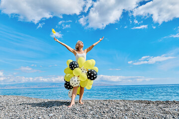 Woman dressed as fairy with yellow and polka dot balloons on pebble beach