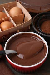 Liquid chocolate dough in bowl and ingredients on wooden table, closeup