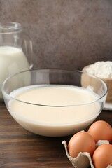 Liquid dough in bowl and ingredients on wooden table, closeup