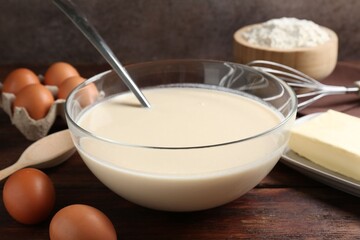 Liquid dough in bowl and ingredients on wooden table, closeup