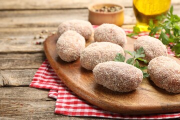 Uncooked meat patties and parsley on wooden table, closeup