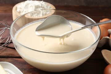 Taking liquid dough from bowl with ladle on wooden table, closeup