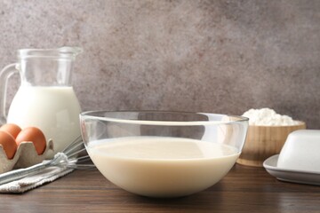 Liquid dough in bowl, whisk and ingredients on wooden table, closeup