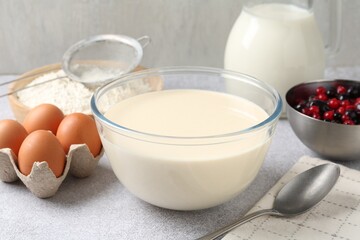 Liquid dough in bowl, berries and ingredients on light grey table, closeup