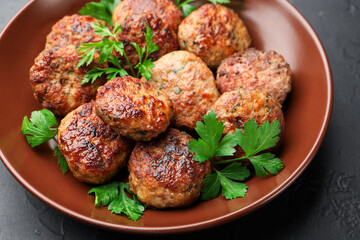 Delicious patties with parsley in bowl on dark textured table, closeup