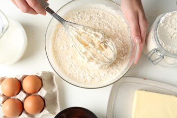 Woman making batter (liquid dough) at white table, top view