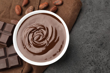 Bowl with melted chocolate, beans and pieces on grey table, flat lay. Space for text