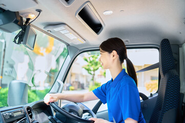 トラックを運転する笑顔の女性ドライバー　配送　引っ越し