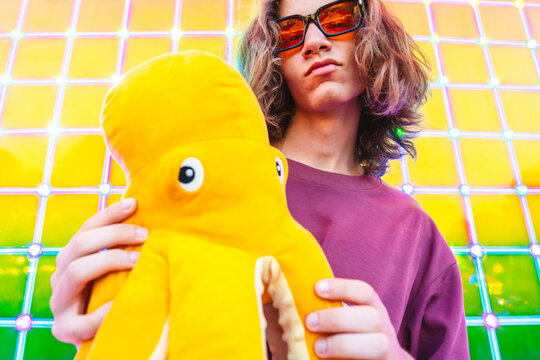 Teenager enjoying neon-lit amusement park holding plush octopus toy