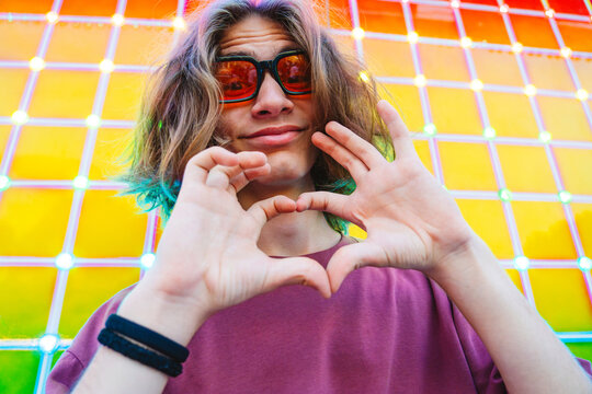 Smiling youth making heart gesture at neon amusement park at night