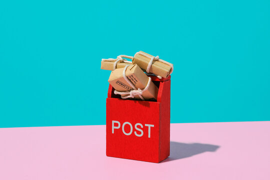 Toy red post box with small paper parcels on pink and blue background