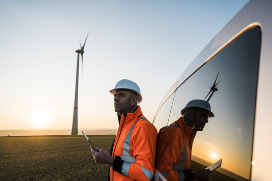 Engineer with tablet inspecting wind turbine at sunset