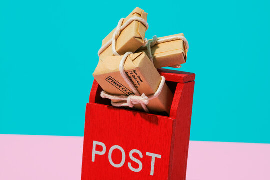 Red toy mailbox with tied cardboard packages on pink and turquoise background