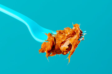 Pulled pork barbecue on blue plastic fork with turquoise background