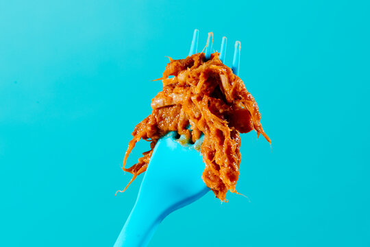Juicy shredded pork on blue fork against turquoise minimal background