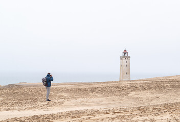 Back view of a standing man photographing Rubjerg Knude lighthouse in Denkmark.