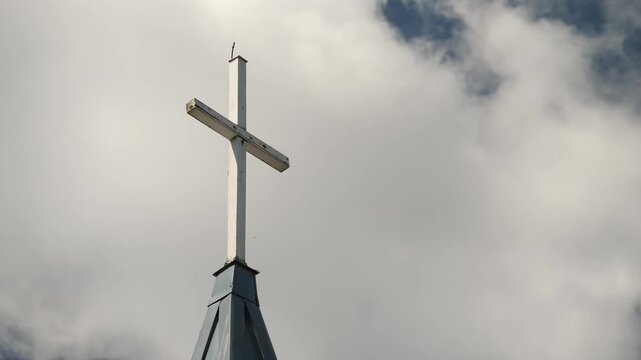 White cross atop church steeple against partly cloudy blue sky