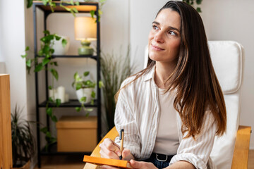 Woman writing in a notebook at home, looking inspired and relaxed