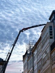 Construction crane extending over scaffolded city building at dusk