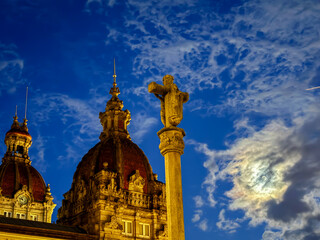 Stone cross and historic domes at dusk with moon