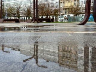 Rain puddle reflecting urban benches and facades