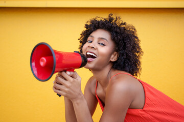 Person with curly afro hairstyle shouting through megaphone against yellow wall