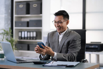 Excited man work distant on computer talk on cellphone celebrate online win. Happy young male use laptop feel euphoric overjoyed triumph with good news over smartphone call.