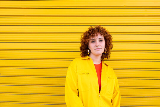 Young woman in urban clothing standing confidently against a yellow corrugated shutter