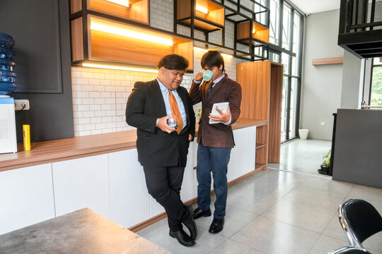 Business Colleagues Review Data On Tablet While Enjoying Coffee In Modern Office Break Room - Powered by Adobe