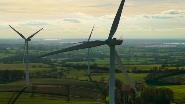 Windmill turbines spinning generating renewable electricity over lush rural landscape. Ecological generators rotating producing sustainable power across vibrant countryside scenery. Alternative energy