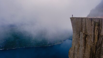 Majestic Preikestolen Cliff stands high above the fjord, shrouded in mist. A solitary figure enjoys...