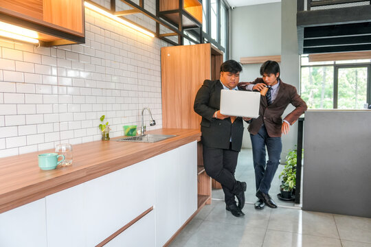 Two Businessmen Collaborate On Laptop In Modern Office Kitchen Discussing Strategy And Success