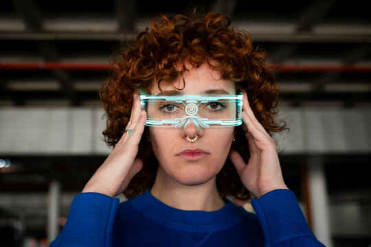 Young woman with curly hair wearing futuristic VR glasses indoors
