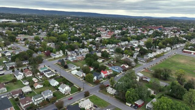 Row of american houses in neighborhood during cloudy morning in autumn. Aerial approaching shot. Green trees and grass field in small town in usa. Quiet and peaceful city town.