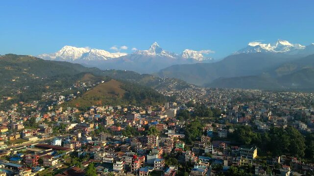 Stunning aerial view of Pokhara city with snow-covered Annapurna and Machhapuchhre peaks in the background, showcasing the beauty of urban life against a Himalayan mountain landscape.