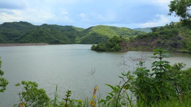 Mountain lake surrounded by lush green hills and vegetation at Presa El Carrizo in Tamazula de Gordiano, Jalisco, Mexico