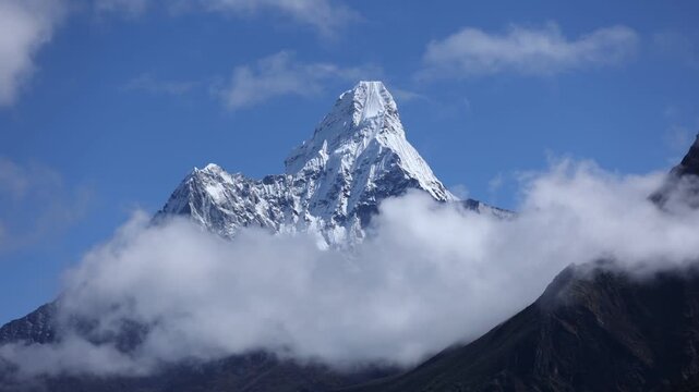 Majestic view of Ama Dablam Mountain in Nepal, its sharp snow-covered summit emerging above drifting clouds against a clear blue sky in the Himalayan range.