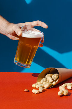 Hand holding glass of beer with peanuts on colorful background