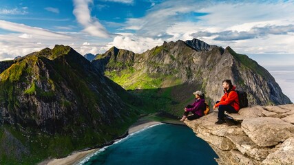 Adventurers relax on a rocky ledge, enjoying stunning views of Ryten Kvalvika Beach and majestic...