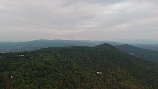 Aerial drone view of J&aacute;nos Hill with the iconic Erzs&eacute;bet Lookout Tower surrounded by lush green forests in the Buda Hills of Budapest, Hungary, under a cloudy sky