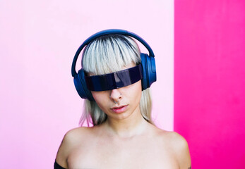 Portrait of woman with futuristic sunglasses and headphones on pink background