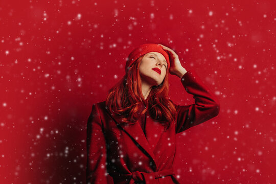 Stylish woman in red coat enjoying falling snow in Christmas mood
