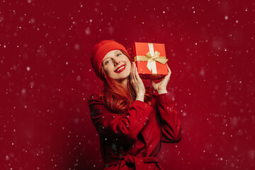 Smiling woman in red holding gift box on red background with falling snow