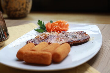 Schweinesteak auf weißem Teller mit Kroketten und Tellerdeko aus Karotten