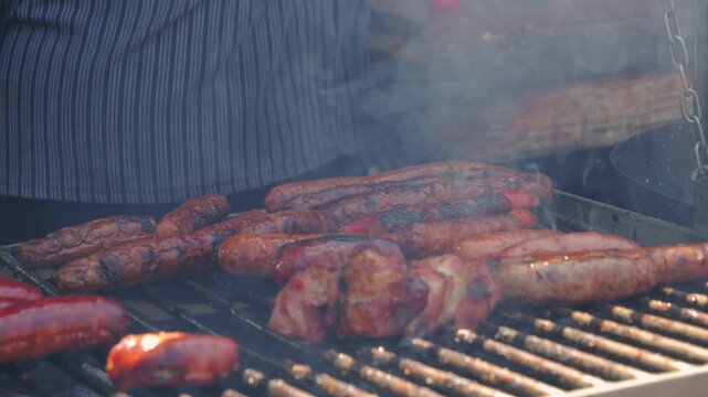 Close-up of grilling sausages on an outdoor barbecue grill in summer, preparing over smoky charcoal. Picnic time with an outdoor grill party. High quality 4k footage