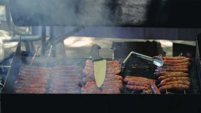 Close-up of grilling sausages on an outdoor barbecue grill in summer, preparing over smoky charcoal. Picnic time with an outdoor grill party. High quality 4k footage