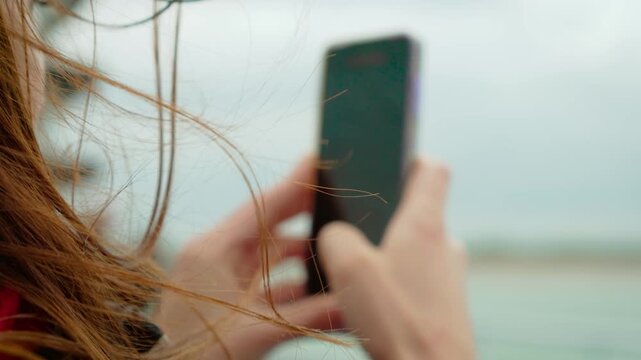 Close up of unrecognizable woman holding smartphone while filming sea from ferry in Dunkirk port France. Wind blowing hair during mobile video capture on ocean ride near harbor. Person recording