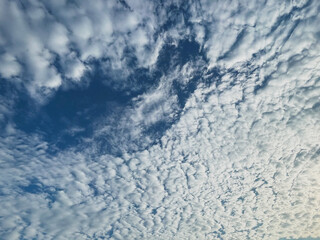 A vibrant blue sky partially covered by a thick layer of textured white clouds, with a clear opening revealing the expanse of the sky.