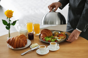 Waiter serving breakfast on wooden table in hotel room, closeup