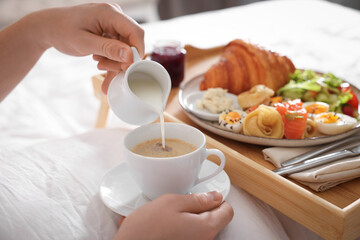 Man pouring cream into coffee while having breakfast in bed, closeup. Hotel room service